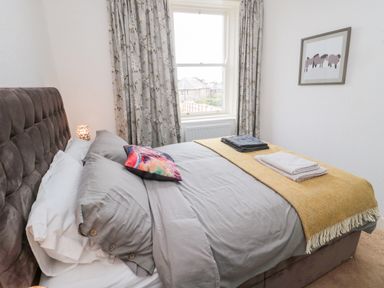 A bedroom with a bed with grey bedding and colorful pillow next to a window with floral curtains at Islestone 1 Temperance Terrace in Berwick-Upon-Tweed