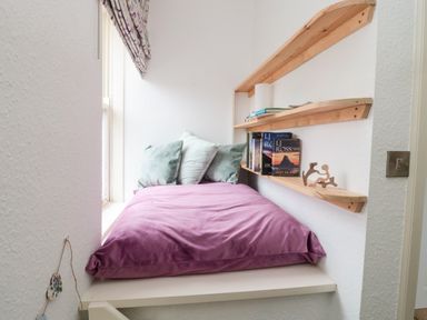 A small nook with a bed covered by a purple blanket and cushions with wooden shelves holding books and decor at Islestone 1 Temperance Terrace in Berwick-Upon-Tweed
