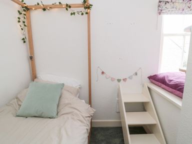 A bedroom with a bed with pillows a wooden frame with string lights a small staircase and a window with a floral curtain at Islestone 1 Temperance Terrace in Berwick-Upon-Tweed