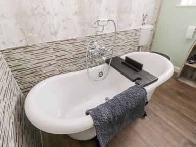 A bathroom with a white freestanding bathtub a black bath tray a gray towel on the tub and floral wallpaper at Islestone 1 Temperance Terrace in Berwick-Upon-Tweed
