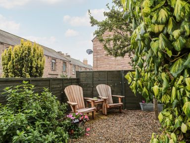 A garden with two wooden chairs and plants at Islestone 1 Temperance Terrace in Berwick-Upon-Tweed