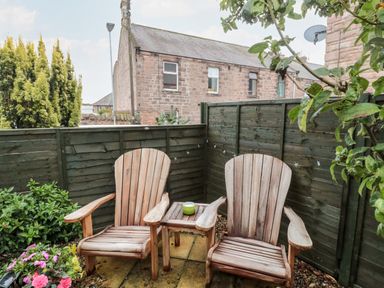 A small outdoor patio with two wooden chairs a small table and flowers behind a green fence at Islestone 1 Temperance Terrace Berwick-Upon-Tweed