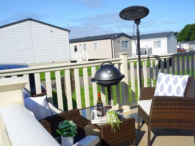 An outdoor patio with wicker chairs a table barbecue grill and a heater at Meadow Lodge in Cayton