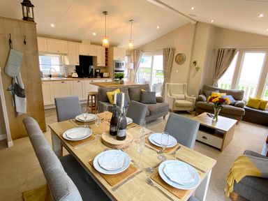 An open-plan dining and living area with a set dining table and a kitchen in the background at Meadow Lodge in Cayton
