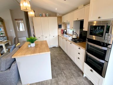 A kitchen with white cabinets wooden countertops a gas stove a microwave an oven a coffee maker and a small island with plants at Meadow Lodge in Cayton