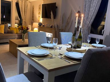 A dining table with plates glasses and candles in a living room with sofas flowers and a television at Meadow Lodge in Cayton