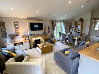 A living room with sofas a dining table and bookshelf at Meadow Lodge in Cayton