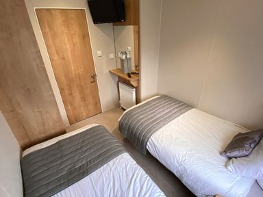 A bedroom with two single beds a wooden door a wall-mounted television and a small shelf with a mirror at Meadow Lodge in Cayton