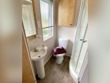 A bathroom with a pedestal sink a toilet with folded towels a corner shower and a wall cabinet at Meadow Lodge in Cayton