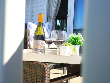 A wicker chair with a tray holding a bottle of wine two glasses and two small plant pots on a patio at Meadow Lodge in Cayton