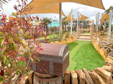An outdoor mini golf course with a wooden treasure chest and covered seating areas at Meadow Lodge in Cayton