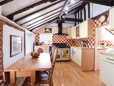 A kitchen with wooden table and chairs a stove and cream cabinets with checkered tiles at The Old Custom House in Wangford