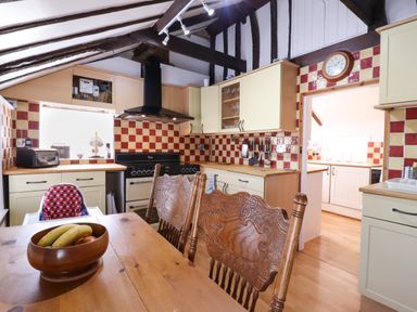 A kitchen with wooden table and chairs a stove and cabinets with red and beige tiles at The Old Custom House in Wangford