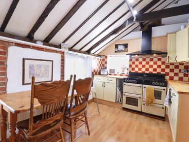 A kitchen with wooden dining table and chairs a stove and checkered tile backsplash at The Old Custom House in Wangford
