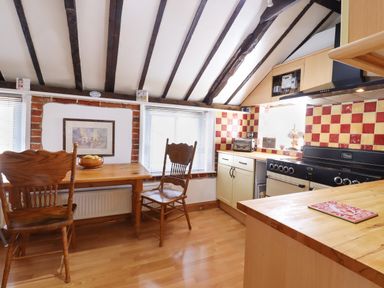 A kitchen with wooden table and chairs next to windows and a stove with red and yellow tiled backsplash at The Old Custom House in Wangford
