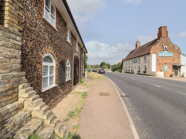 A street view with a stone building on the left and a pub called The White Hart Inn on the right at The Old Custom House in Wangford