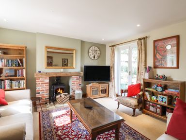 A living room with a brick fireplace, a wooden coffee table on a patterned rug and bookshelves at The Old Custom House in Wangford