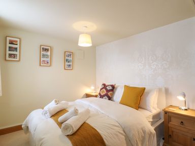 A bedroom with a bed with rolled towels on it two bedside tables with lamps and framed pictures on the wall at The Old Custom House in Wangford