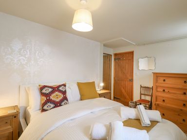 A bedroom with a bed with pillows and towels a wooden dresser a wooden door and a chair at The Old Custom House in Wangford