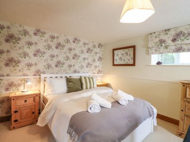 A bedroom with a bed with rolled towels bedside tables a window and floral wallpaper at The Old Custom House in Wangford