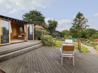 A wooden deck with a table and two chairs next to a garden with trees and shrubs at The Old Custom House in Wangford