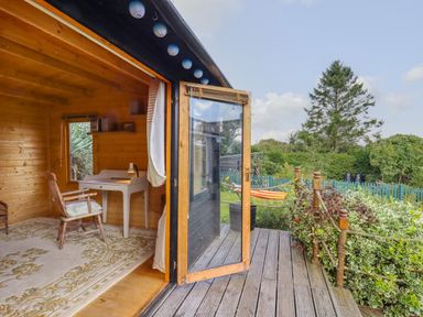 A wooden garden room with a desk and chair opening onto a wooden deck and garden at The Old Custom House in Wangford