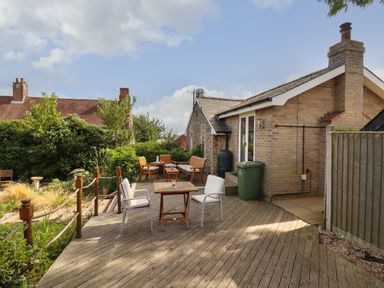 A wooden deck with chairs and tables next to a brick house and a garden at The Old Custom House in Wangford