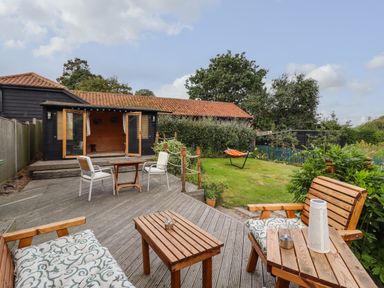 An outdoor wooden deck with chairs and tables leading to a garden with grass and a hammock at The Old Custom House in Wangford