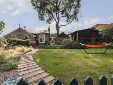 A backyard with a wooden pathway grass lawn hammock and small buildings at The Old Custom House in Wangford