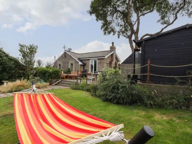 A backyard with a red and yellow striped hammock lawn bushes a wooden deck with chairs and a house at The Old Custom House in Wangford