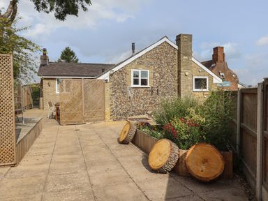 An outdoor patio area with a flower bed and tree stumps next to a building made of stone and brick at The Old Custom House in Wangford
