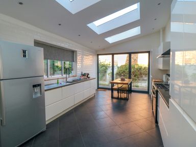 A kitchen with a refrigerator a sink a stove a wooden dining table with benches and large windows at South Bay House in Scarborough