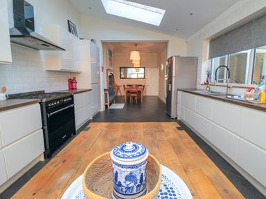 A kitchen with white cabinets and black appliances leading to a dining area with wooden table and chairs at South Bay House in Scarborough
