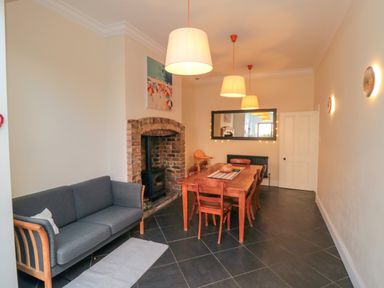 A dining room with a wooden table and chairs a gray sofa and a brick fireplace at South Bay House in Scarborough