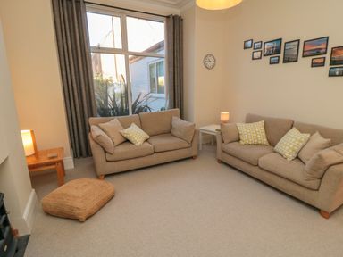 A living room with two beige sofas with cushions a large window cushions on the floor lamps wood side tables a clock and picture frames on the wall at South Bay House in Scarborough