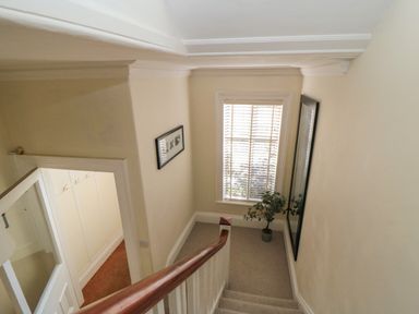 A staircase with a wooden handrail leading to a landing with a window plant and mirror at South Bay House in Scarborough
