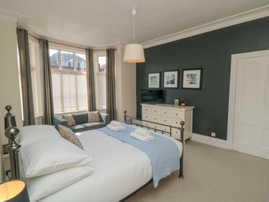 A bedroom with a double bed and white dresser with TV on a dark accent wall at South Bay House in Scarborough
