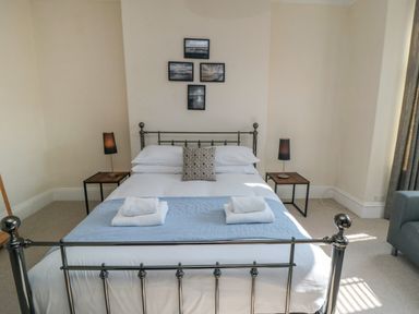 A bedroom with a metal bed frame two bedside tables with lamps and framed pictures on the wall at South Bay House in Scarborough