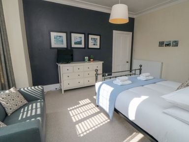 A bedroom with a bed with towels on it a sofa a dresser with a TV and pictures on the wall at South Bay House in Scarborough