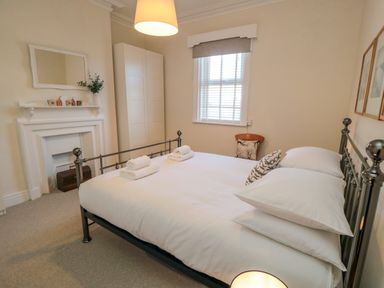 A bedroom with a metal bed frame white bedding towels on bed a chair by the window a fireplace with a mirror above and a wardrobe at South Bay House in Scarborough