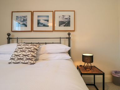 A bed with white bedding and a pillow with dragonfly designs next to a wooden side table with a black lamp at South Bay House in Scarborough