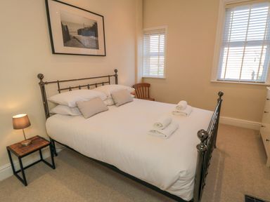 A bedroom with a double bed two windows bedside table with lamp wooden chair and chest of drawers at South Bay House in Scarborough