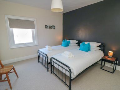 A bedroom with two single beds with blue pillows and white linens a wooden chair near a window and a bedside table with a lamp at South Bay House in Scarborough