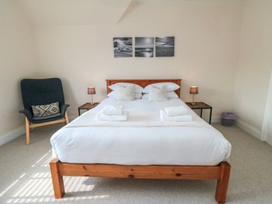 A bedroom with a wooden bed frame two bedside tables with lamps and a chair at South Bay House in Scarborough