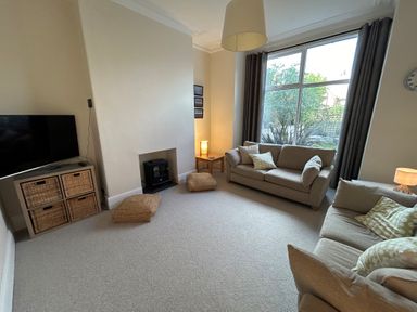 A living room with two sofas cushions a TV on a stand with wicker drawers and a window at South Bay House in Scarborough
