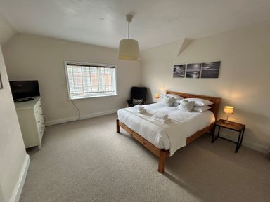 A bedroom with a wooden bed two bedside tables two lamps a chair a dresser with a television and a window with blinds at South Bay House in Scarborough