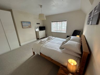 A bedroom with a double bed towels on bed bedside lamp armchair window dresser with TV and wardrobe at South Bay House in Scarborough