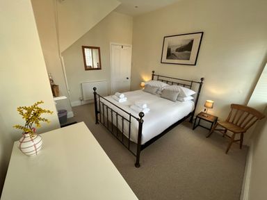 A bedroom with a metal bed frame white bedding rolled towels bedside tables with lamps a wooden chair a mirror and a vase with yellow flowers at South Bay House in Scarborough