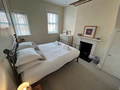 A bedroom with a metal frame bed pillows and towels a white dresser a fireplace and two windows at South Bay House in Scarborough