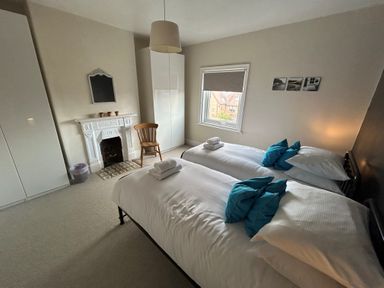 A bedroom with two single beds with white linens and blue pillows a wooden chair and a decorative fireplace at South Bay House Scarborough